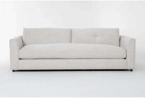 The Thea Down 101 Inch Beige Chenille Sofa, featuring a minimal design, is set against a plain white background. This modern piece includes two large back cushions and low, blocky armrests for a contemporary look.