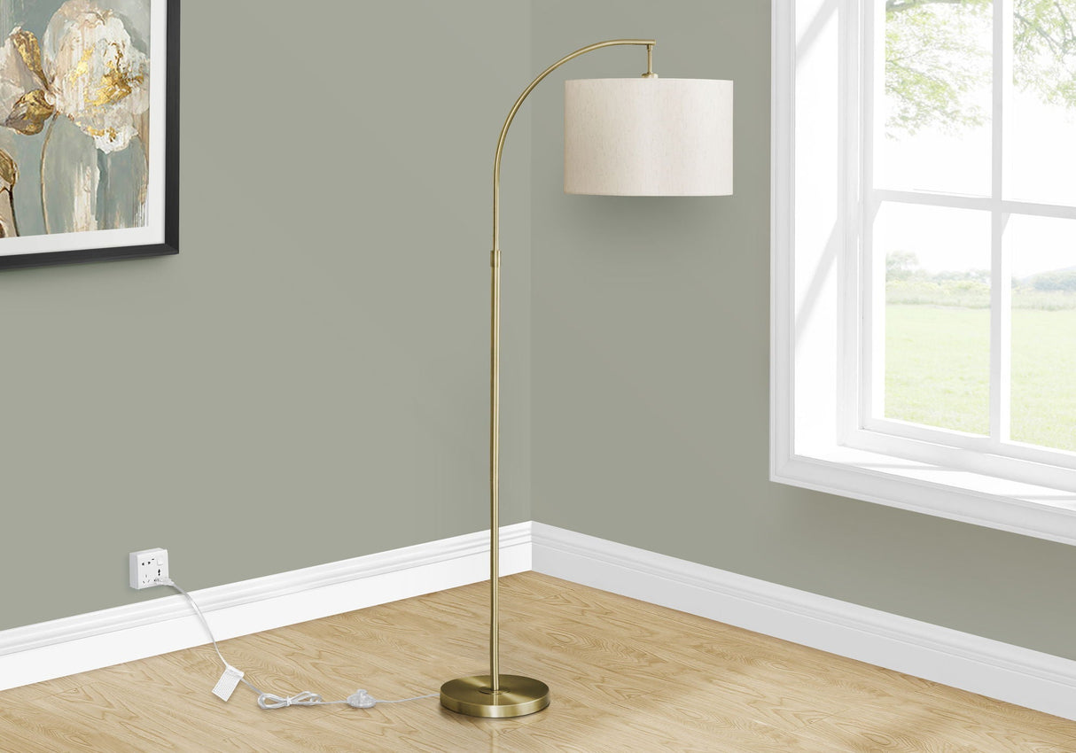 The Contemporary Design Floor Lamp Lighting, featuring a curved brass-colored stand and a white cylindrical shade, sits by a large window on a wooden floor against a light green wall, with its power cord plugged into an outlet.