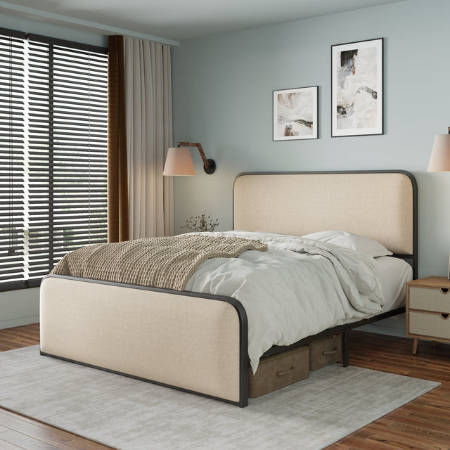 A modern bedroom features a curved beige upholstered bed with white bedding and a knitted throw. Two abstract paintings hang above. To the left, a window with closed blinds and beige curtains. A wooden nightstand with a lamp sits by the bed on a light gray rug.