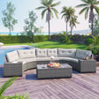 An 8-piece outdoor wicker round sofa set with a half-moon sectional and gray cushions sits on a wooden deck. A rectangular coffee table holds snacks and drinks. Palm trees, hedges, and a swimming pool enrich the scene with views of water and distant mountains in the background.