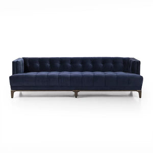 Introducing the Dylan Sofa by Four Hands, a sophisticated and contemporary piece featuring navy blue velvet upholstery with deep button tufting. Its design includes dark wooden legs and a rectangular shape with low back and armrests, all set against a plain white background.