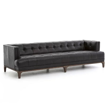 The Dylan Sofa by Four Hands is a contemporary black leather piece featuring a tufted design with deep button detailing and squared armrests. It rests on a wooden base with short legs and is showcased against a plain white background.