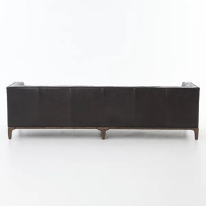 The Dylan Sofa by Four Hands, in dark leather, is showcased from the back to highlight its sleek and modern design with clean lines. It features four tapered wooden legs, all set against a plain white background.