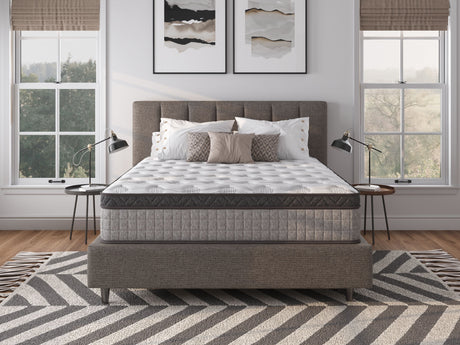 A modern bedroom showcases a large upholstered bed with a 12" Diamond Innerspring Hybrid and Cooling Gel Memory Foam Mattress. It includes two bedside tables with lamps, abstract art, windows with beige blinds, and a gray zigzag-patterned rug on the wooden floor.