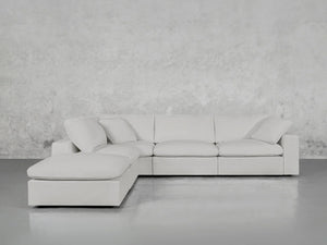 The 5-Seat Modular Corner Lounger Sectional, in light gray, is positioned against a textured gray wall on a smooth gray floor. It features plush cushions and boasts a minimalist design.