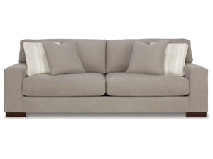 The Maggie Sofa, in light gray, showcases a modern design with sleek lines and wooden feet. It comes with two matching cushions and two striped accent pillows, all set against a plain white background.