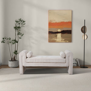 A minimalist living room with the Regent Bench in cream, cylindrical cushions, a tall potted plant on the left, a modern floor lamp on the right, and a sunset over water painting on the back wall.