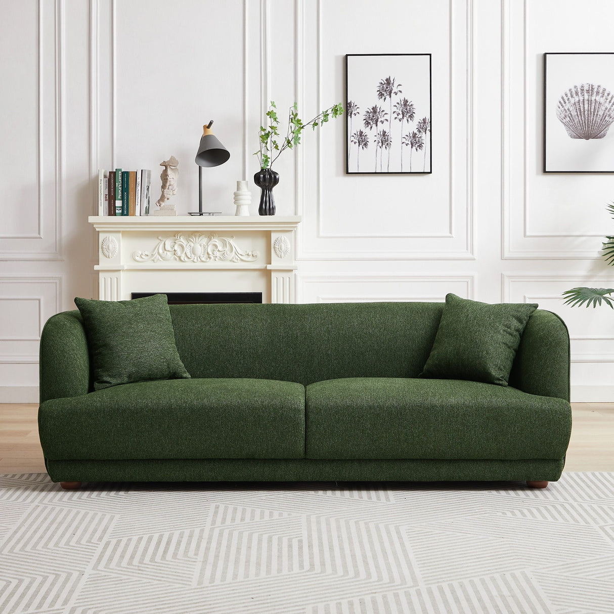 A modern living room features the Larisa Mid-Century Modern Linen Sofa in green, positioned before a decorative white fireplace. Black-and-white art adorns the wall. A small plant offers greenery, while a patterned rug enhances the floor, creating a cozy and stylish atmosphere.