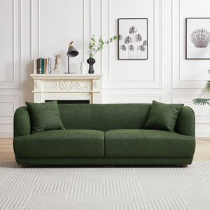 A modern living room features the Larisa Mid-Century Modern Linen Sofa in green, positioned before a decorative white fireplace. Black-and-white art adorns the wall. A small plant offers greenery, while a patterned rug enhances the floor, creating a cozy and stylish atmosphere.