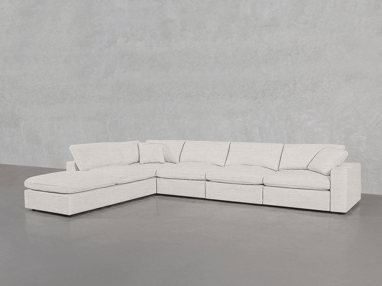 The 6-Seat Modular Corner Lounger Sectional features light beige fabric upholstery and a left-side chaise, shown against a plain light gray wall and floor.