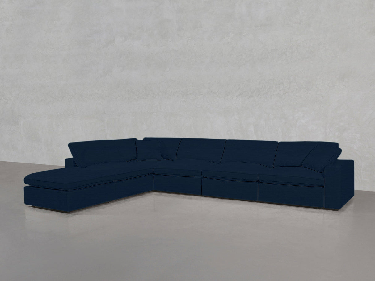 The 6-Seat Modular Corner Lounger Sectional, in dark blue with wide cushions, is set on a smooth light gray floor against a textured light gray wall.