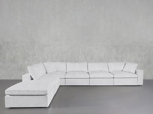 A 6-Seat Modular Corner Lounger Sectional in light gray, featuring plush cushions and a left-side chaise, is set against a plain gray textured wall and floor.