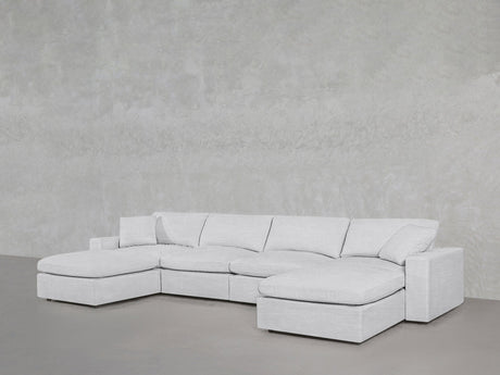 A 6-Seat Modular Double Chaise Sectional in light gray with plush cushions sits on a smooth gray floor against a textured light gray wall.