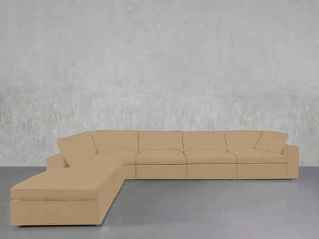 A 6-Seat Modular Corner Lounger Sectional in beige, featuring multiple cushions, is arranged against a plain light-gray textured wall on a smooth gray floor.