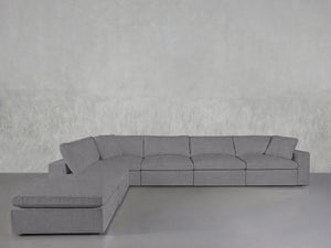 The 6-Seat Modular Corner Lounger Sectional in light gray, featuring plush cushions, is arranged on a smooth gray floor against a textured light gray wall.