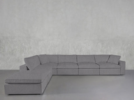 The 6-Seat Modular Corner Lounger Sectional in light gray, featuring plush cushions, is arranged on a smooth gray floor against a textured light gray wall.