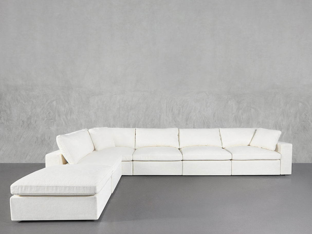 The 6-Seat Modular Corner Lounger Sectional, featuring plush cushions and a modern white finish, is placed against a light gray textured wall and a smooth gray floor.