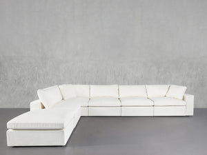 The 6-Seat Modular Corner Lounger Sectional, featuring plush cushions and a modern white finish, is placed against a light gray textured wall and a smooth gray floor.