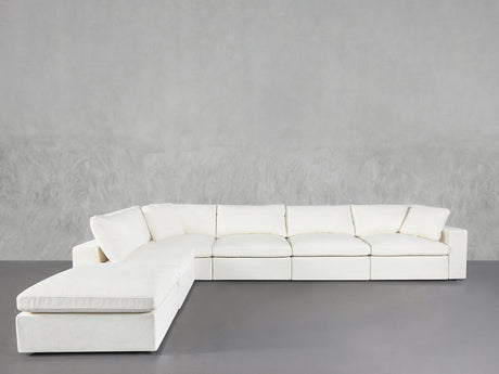 The 6-Seat Modular Corner Lounger Sectional, featuring plush cushions and a modern white finish, is placed against a light gray textured wall and a smooth gray floor.