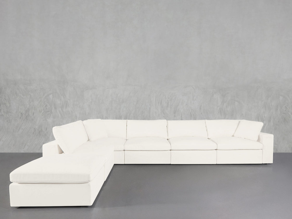 The 6-Seat Modular Corner Lounger Sectional, featuring a modern white design with clean lines and plush cushions, is arranged against a textured light gray wall and a smooth gray floor.