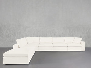 The 6-Seat Modular Corner Lounger Sectional, featuring a modern white design with clean lines and plush cushions, is arranged against a textured light gray wall and a smooth gray floor.