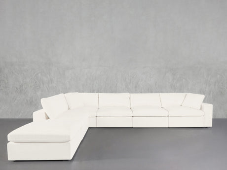 The 6-Seat Modular Corner Lounger Sectional, featuring a modern white design with clean lines and plush cushions, is arranged against a textured light gray wall and a smooth gray floor.