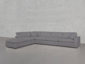 A spacious 6-Seat Modular Corner Lounger Sectional in light gray with wide cushions and a chaise lounge is placed on a smooth concrete floor against a textured light gray wall.
