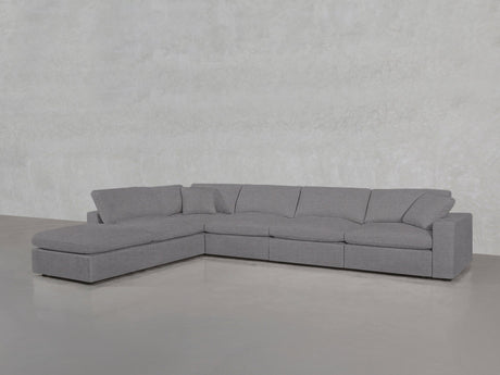 A spacious 6-Seat Modular Corner Lounger Sectional in light gray with wide cushions and a chaise lounge is placed on a smooth concrete floor against a textured light gray wall.