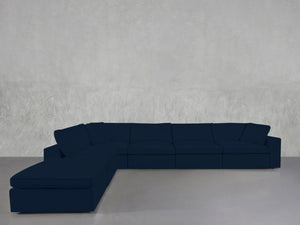 A 6-Seat Modular Corner Lounger Sectional in dark blue is arranged against a plain light gray wall and floor in a minimalist room.