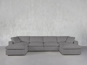 The 6-Seat Modular Double Chaise Sectional in modern gray, featuring wide armrests and cushions, sits against a light gray textured wall in a minimalist space.