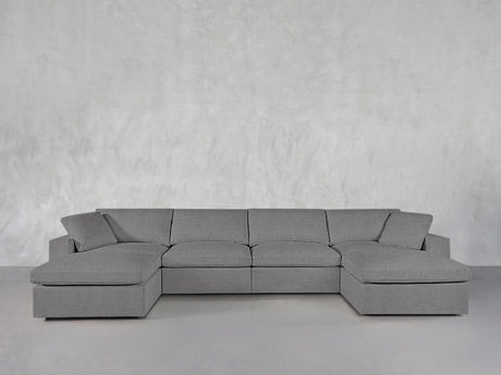 The 6-Seat Modular Double Chaise Sectional in modern gray, featuring wide armrests and cushions, sits against a light gray textured wall in a minimalist space.