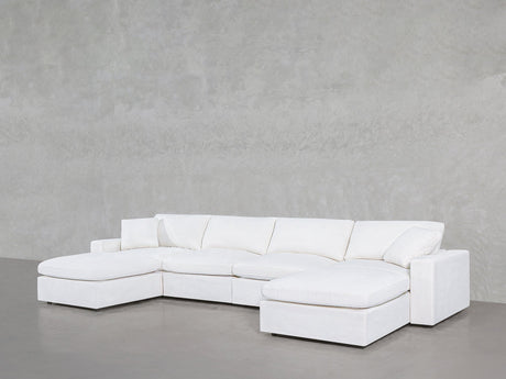 The 6-Seat Modular Double Chaise Sectional, featuring clean lines and plush cushions, is arranged against a light gray textured wall on a smooth floor.