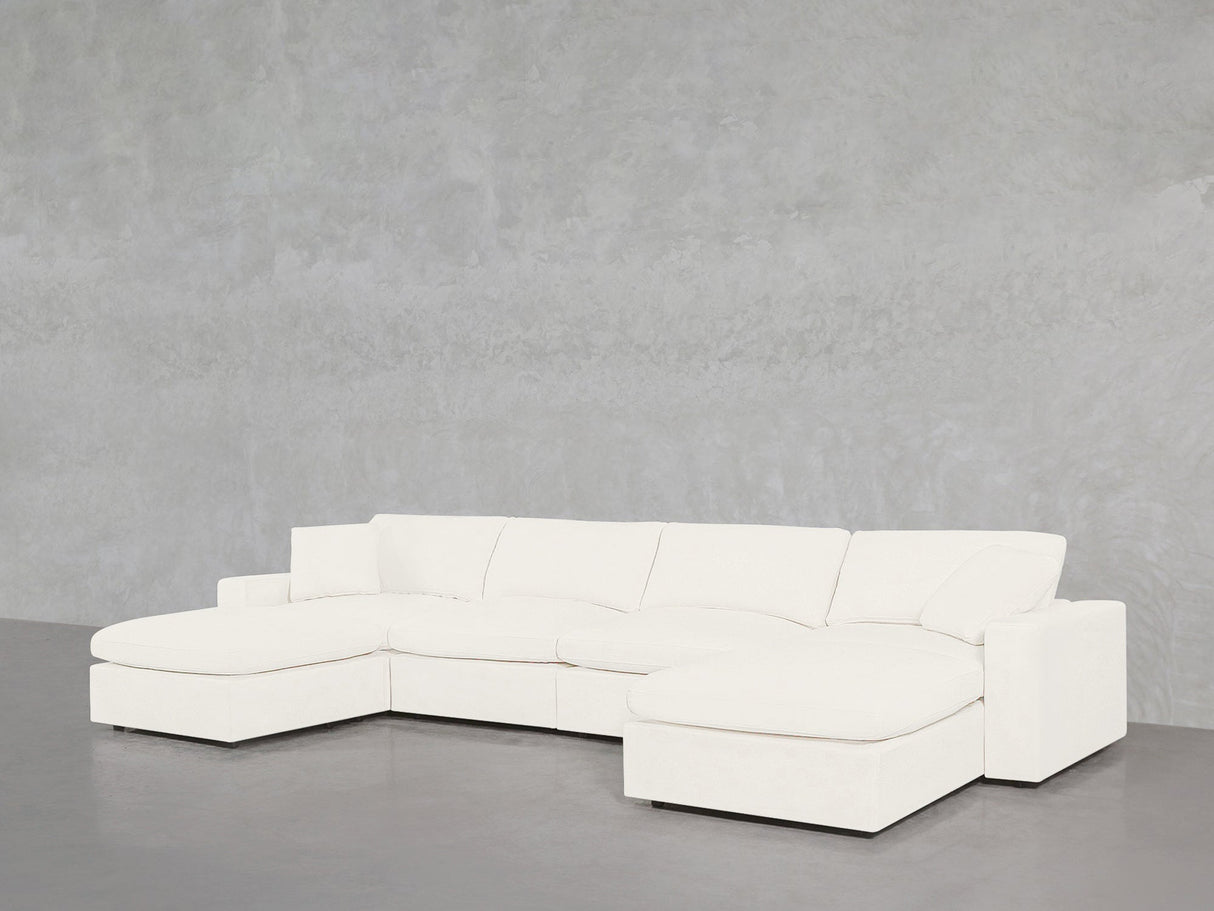 The 6-Seat Modular Double Chaise Sectional, featuring a modern white design with clean lines, wide armrests, and plush cushions, sits against a light gray textured wall and smooth gray floor, with a chaise lounge on the left side.