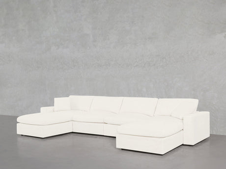 The 6-Seat Modular Double Chaise Sectional, featuring a modern white design with clean lines, wide armrests, and plush cushions, sits against a light gray textured wall and smooth gray floor, with a chaise lounge on the left side.