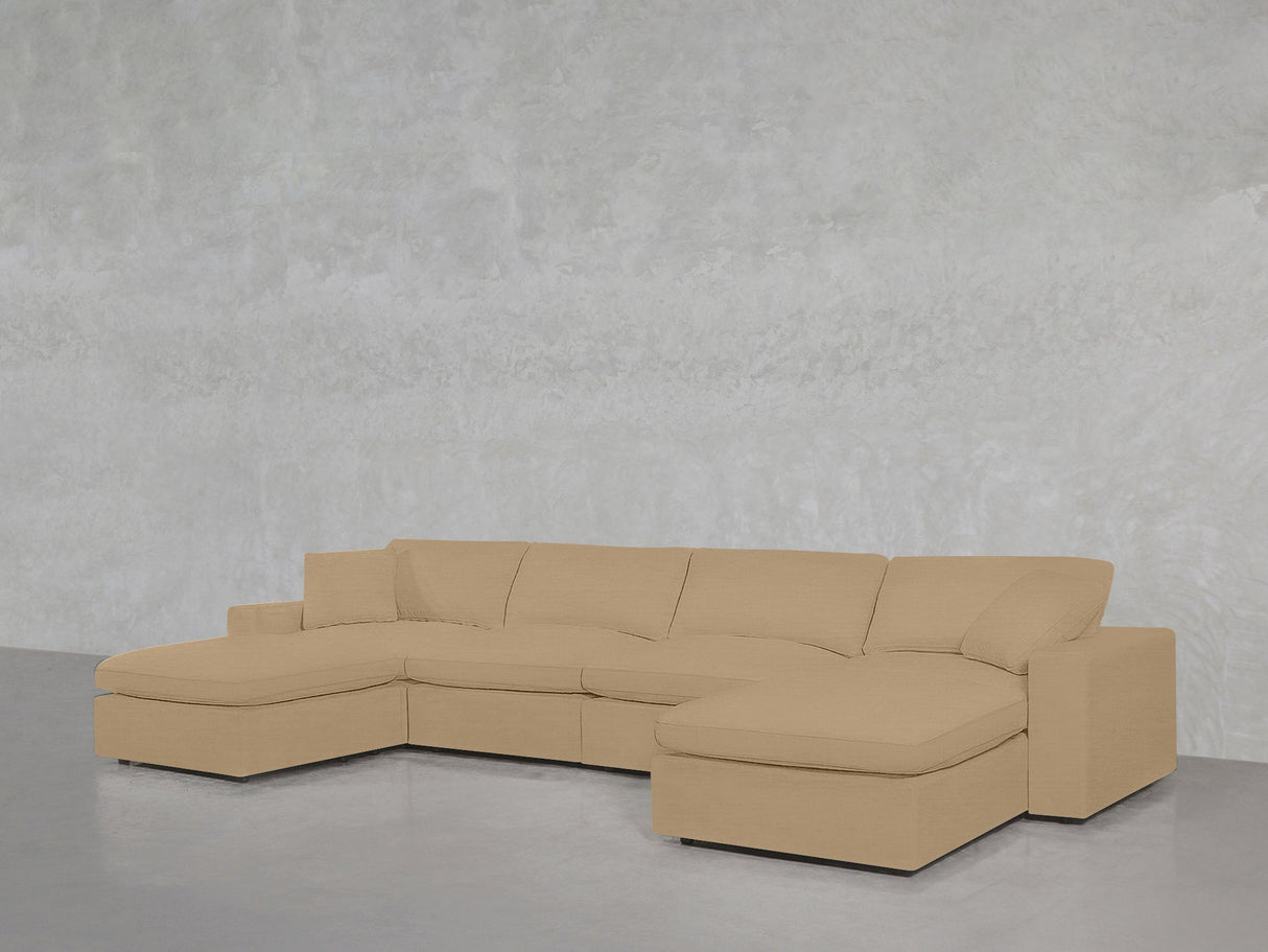 The 6-Seat Modular Double Chaise Sectional in beige features wide cushions and chaise lounges at both ends, positioned against a light grey textured wall and a glossy grey floor.