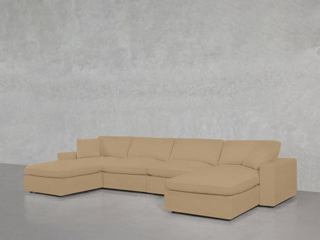 The 6-Seat Modular Double Chaise Sectional in beige features wide cushions and chaise lounges at both ends, positioned against a light grey textured wall and a glossy grey floor.