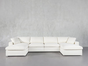 The 6-Seat Modular Double Chaise Sectional, featuring wide seats, plush cushions, and chaise lounges on both ends, is showcased against a plain light gray wall and a smooth gray floor.