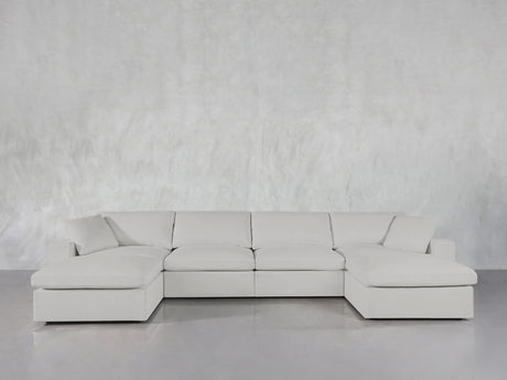 The 6-Seat Modular Double Chaise Sectional with clean lines and plush cushions is arranged in front of a light gray textured wall on a glossy floor.
