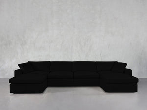The 6-Seat Modular Double Chaise Sectional, featuring wide seats and low backrests in modern black, is arranged against a light gray textured wall and a smooth, reflective floor.