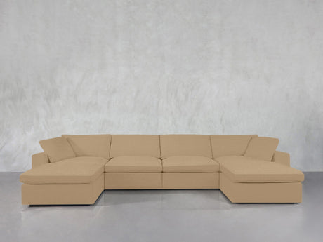 A 6-Seat Modular Double Chaise Sectional in beige sits against a light gray textured wall, with its two chaise lounges on either end. The floor beneath is smooth and reflective.