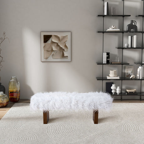 A modern living room showcases the Henley Fur Bench in White Khaki on a textured rug, with a geometric art piece on a light gray wall. A black metal shelf to the right holds decorative items, while a large glass vase rests on the floor to the left.