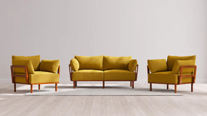A stylish living room arrangement featuring the Indoor Jack 2-Seater Sofa + Armchair Set in Balsa, showcasing a mustard yellow sofa accompanied by two matching armchairs. They rest elegantly on a light beige rug over a light wood floor, with wooden frames accentuating the furniture against a plain wall backdrop.