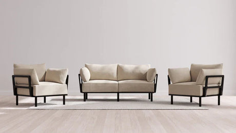 A contemporary living room ensemble featuring the Indoor Jack 2-Seater Sofa + Armchair Set in Balsa, showcasing a beige hue with sleek black frames. The set is tastefully placed on a light area rug within a bright, minimalist space adorned with wooden floors.