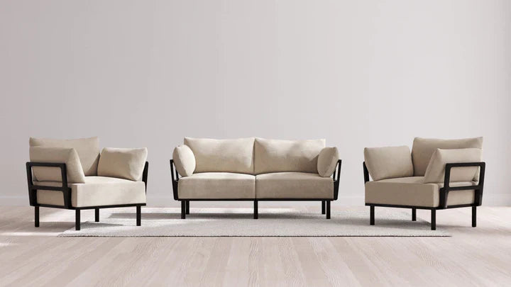 A contemporary living room ensemble featuring the Indoor Jack 2-Seater Sofa + Armchair Set in Balsa, showcasing a beige hue with sleek black frames. The set is tastefully placed on a light area rug within a bright, minimalist space adorned with wooden floors.