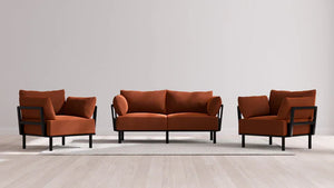 A contemporary living room ensemble showcases the Indoor Jack 2-Seater Sofa and Armchair Set in a warm Balsa shade. They are paired with black-framed armchairs, all positioned on a light gray rug atop a wooden floor against a plain gray wall.