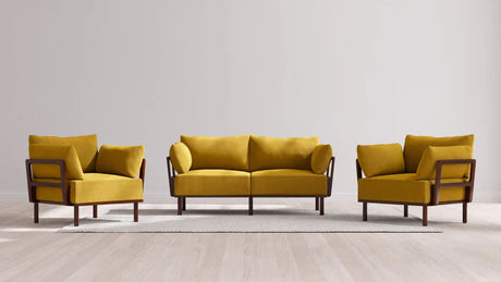 A contemporary living room arrangement showcasing the Indoor Jack 2-Seater Sofa and two matching armchairs in a warm mustard yellow Balsa color. The furniture, with its stylish wooden frames, is elegantly placed on a light-colored rug against a plain white wall and light wood flooring.