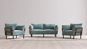 A minimalist living room arrangement featuring the Indoor Jack 2-Seater Sofa + Armchair Set in Balsa, showcasing a pair of matching armchairs and a two-seater sofa with light blue-green cushions and dark wooden frames, all placed on a light-colored area rug over a wooden floor.