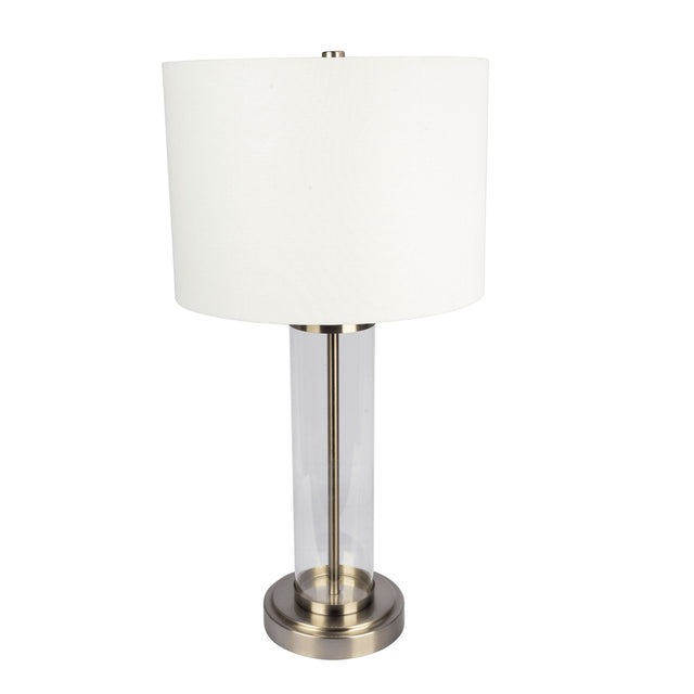 The Luna table lamp features a cylindrical clear glass base with a brushed metal bottom, white drum shade, and central metal rod topped by a metallic finial.
