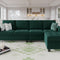 A modern living room features the Belffin Reversible Sectional Convertible Storage sofa, which is green and decorated with striped and geometric pillows. A white and green patterned rug covers the floor, while in the background, you can see a kitchen with white cabinetry and pendant lights.