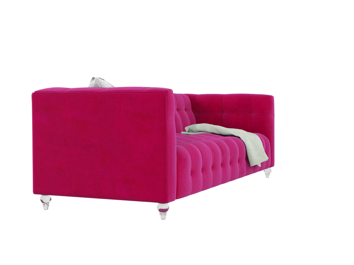 The Bea Velvet Tufted Sofa in a vibrant pink color, featuring clear legs, is angled to the left. A light green textured blanket is draped over one side. The background is white.
